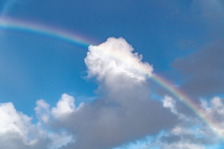 Ein bunter Regenbogen am blauen Himmel mit weißen Wolken